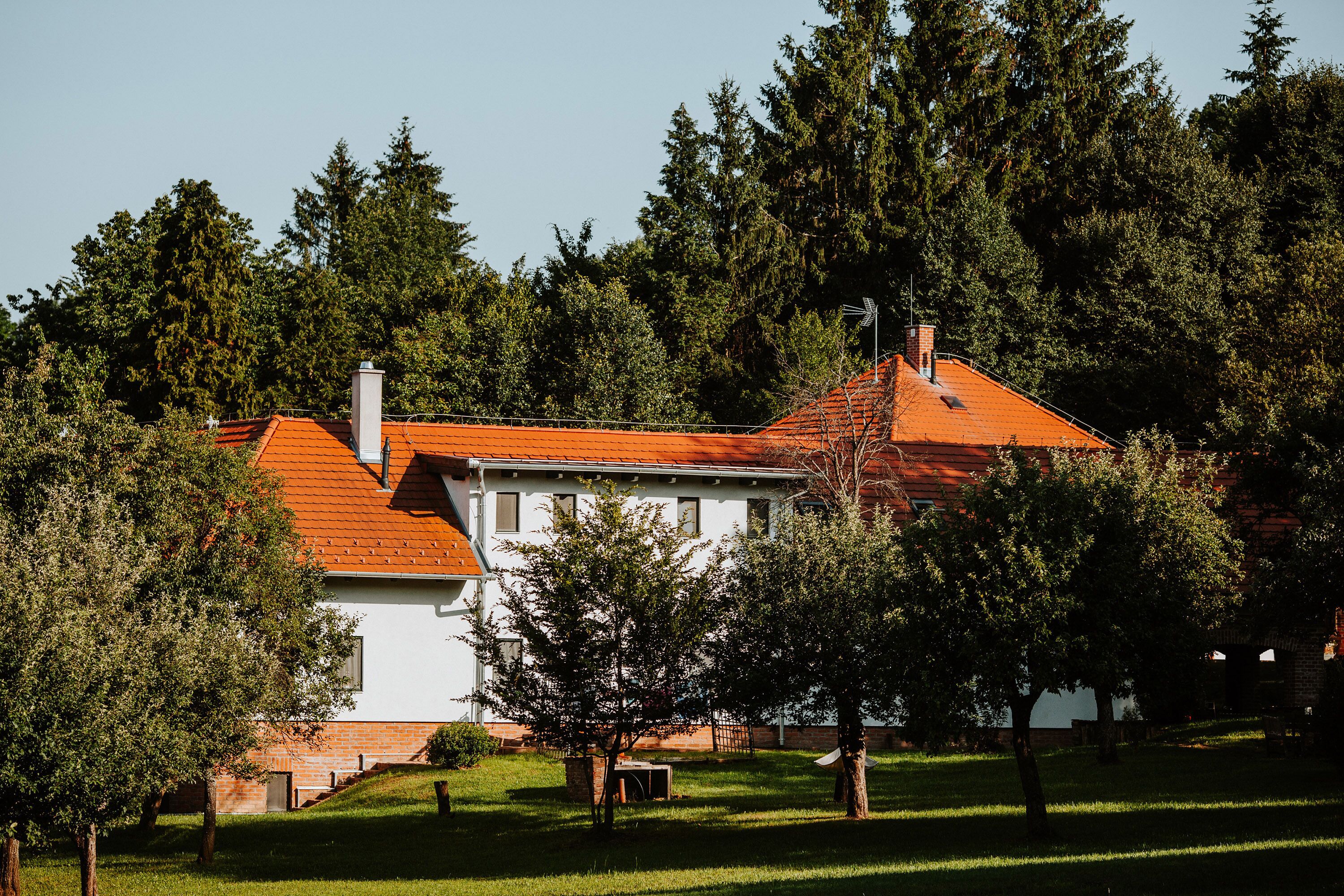 A white building with a red roof, surrounded by trees and grass.
