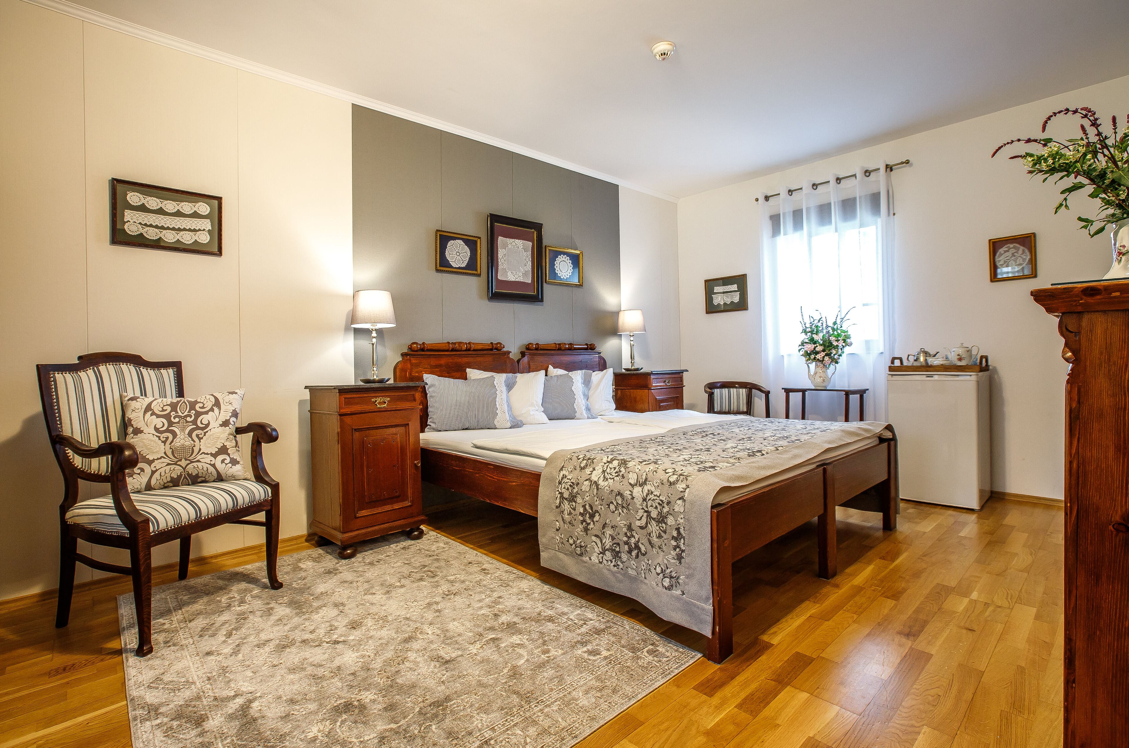 Un dormitorio con una cama de madera, una silla, una mesita de noche, un aparador y una pequeña mesa con una planta.