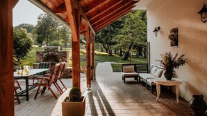 An outdoor patio with a brick fireplace, wooden furniture, and a view of a garden. - Kosbor Panzió (Magyarszombatfa)