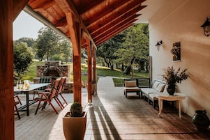 Un patio exterior con chimenea de ladrillo, mobiliario de madera y vistas a un jardín.