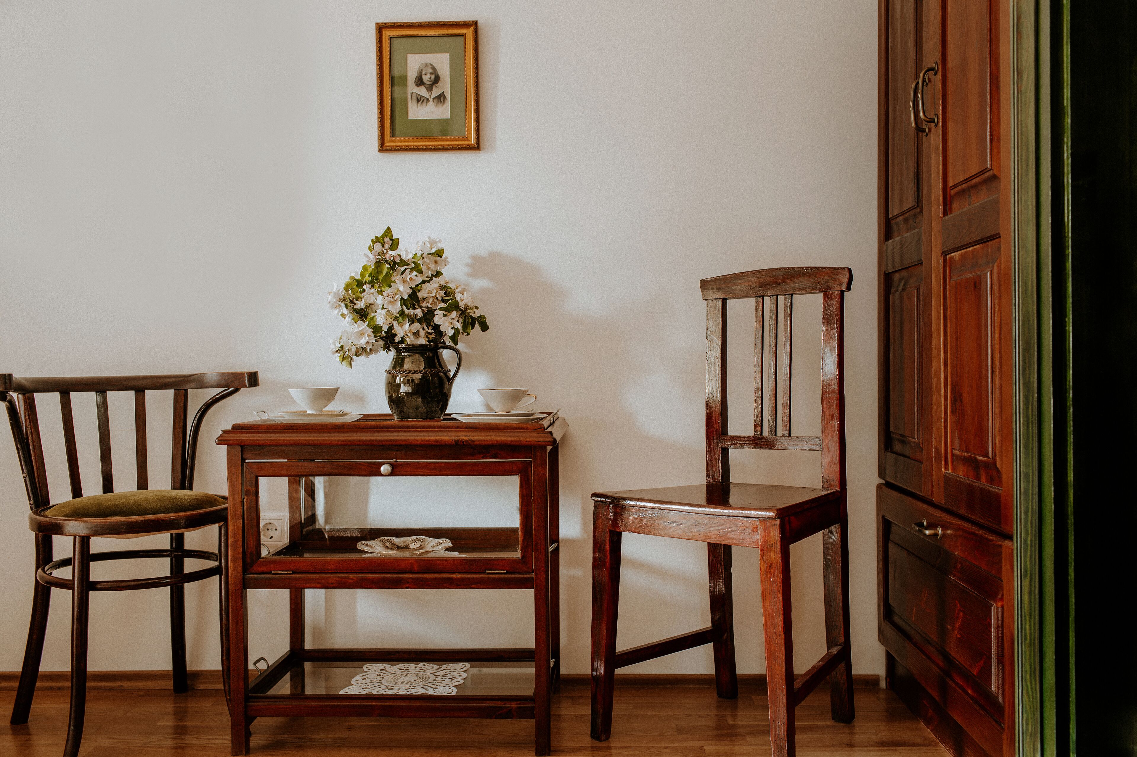 A wooden table with a vase of flowers, two chairs, and a cabinet.