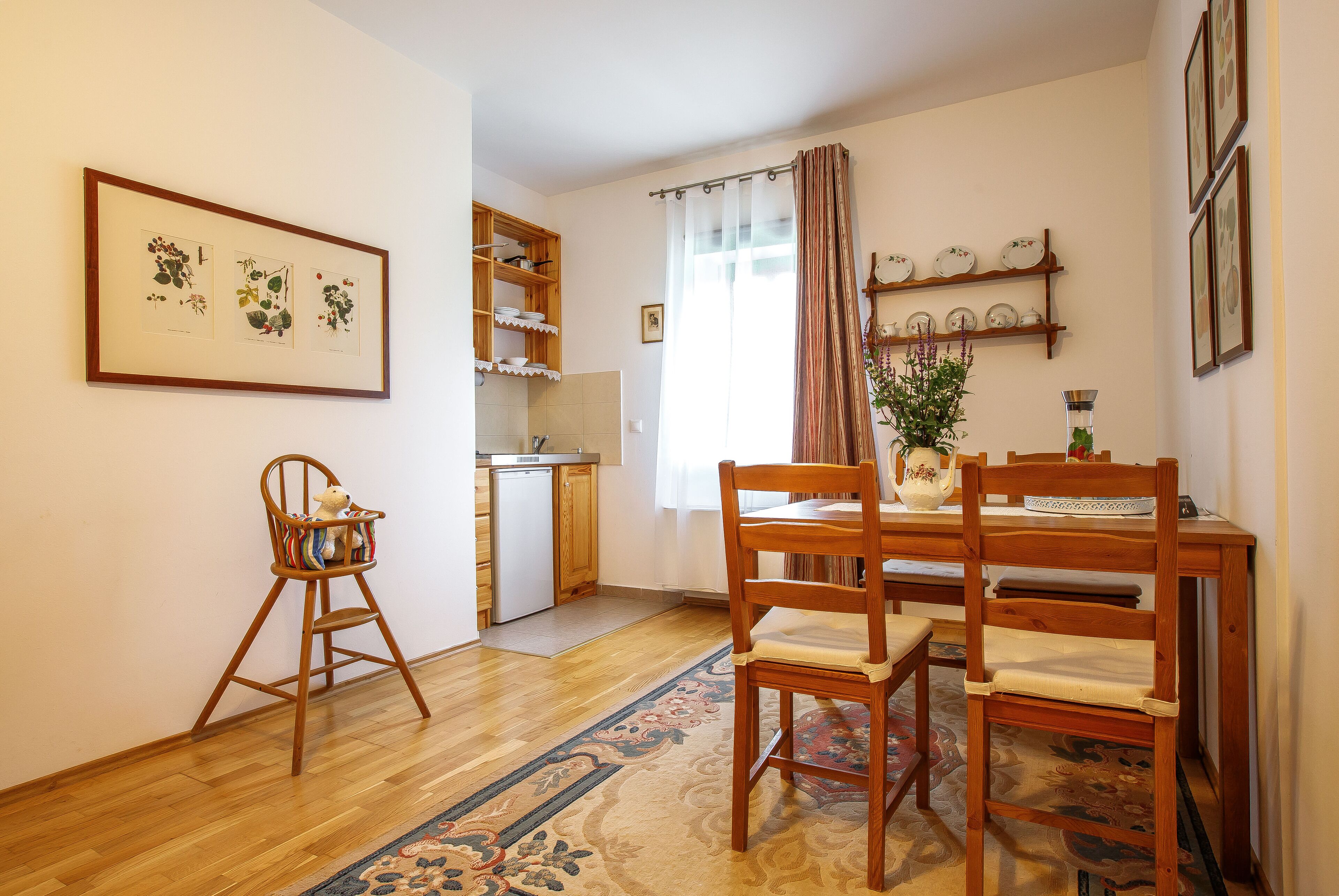 A dining area with a wooden table, chairs, a rug, and a baby rocker.