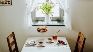 A table set with pastries, tea, and a floral arrangement by a window with sheer curtains. - Kosbor Panzió (Magyarszombatfa)