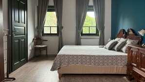 A bedroom with a bed, two windows with curtains, a chair, a wooden dresser, and a door. - Kosbor Panzió (Magyarszombatfa)