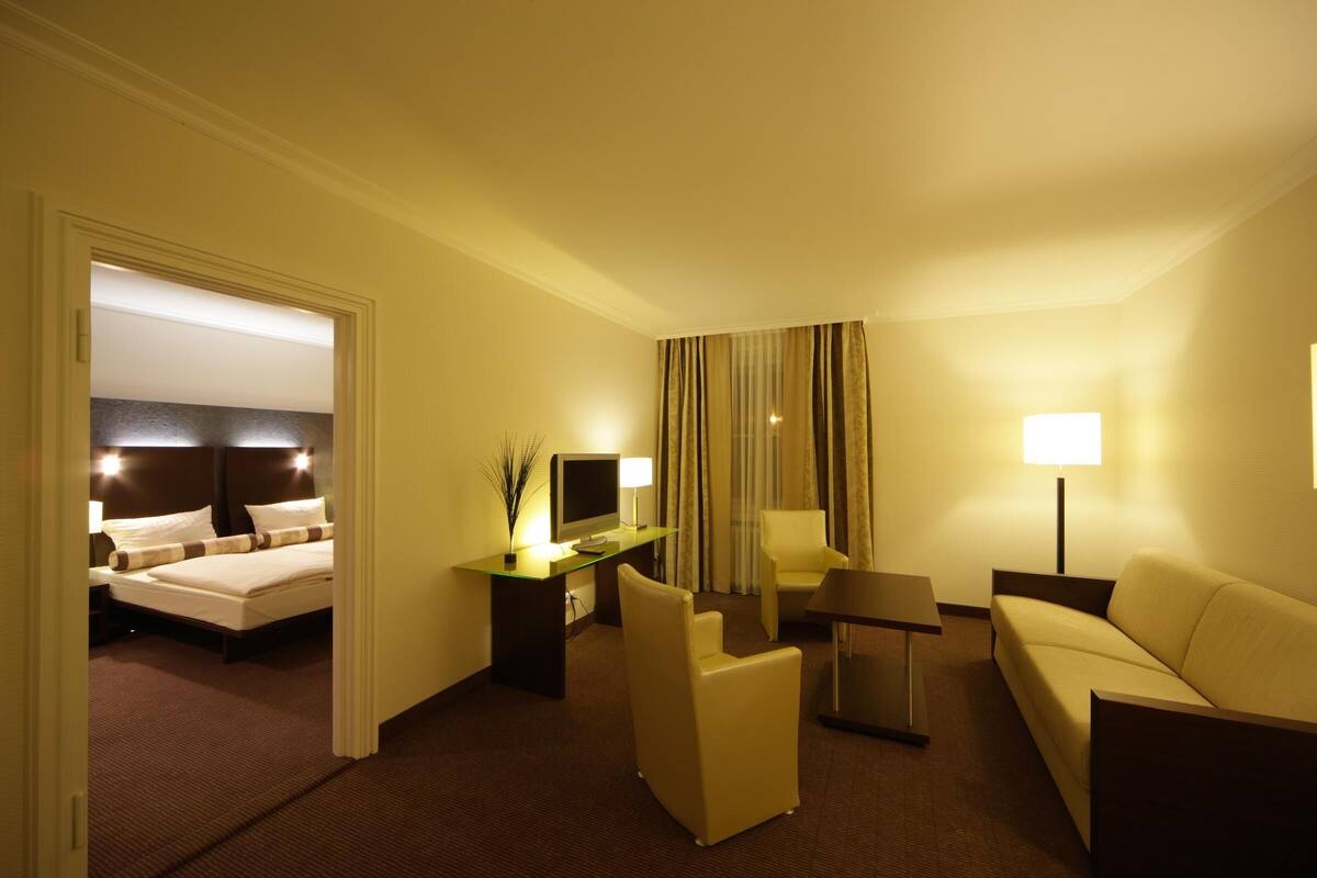 Hotellihuone, jossa on sänky, työpöytä tietokoneella, sohva ja tuoli.