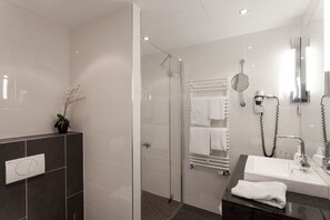 A modern bathroom with a glass-enclosed shower, a vanity with a sink, and a towel rack. - Hotel Am See (Salzgitter)