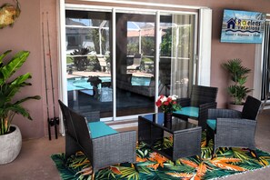 A patio area with wicker furniture, a glass table, and a tropical-themed rug.