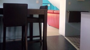 Ein Essbereich mit Tisch und Stühlen, eine rote Couch im Hintergrund und eine Treppe, die zu einer anderen Ebene führt.