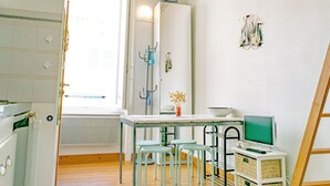 A compact kitchen with a dining area, a radiator, a computer on a small table, and a window with a view. - Cozy Studio Near Beach and Downtown (Les Sables-d'Olonne)