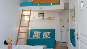 A compact room with a bunk bed, a desk with a chair, a small table with a vase, and a door with a towel hanging on it. - Cozy Studio Near Beach and Downtown (Les Sables-d'Olonne)