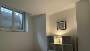 Un dormitorio con una cama individual, una ventana, una estantería con una lámpara y un cuadro en la pared.