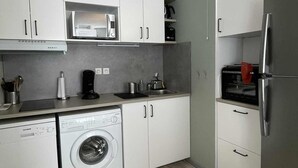 A compact kitchen with white cabinets, a stainless steel refrigerator, a washing machine, and a microwave.