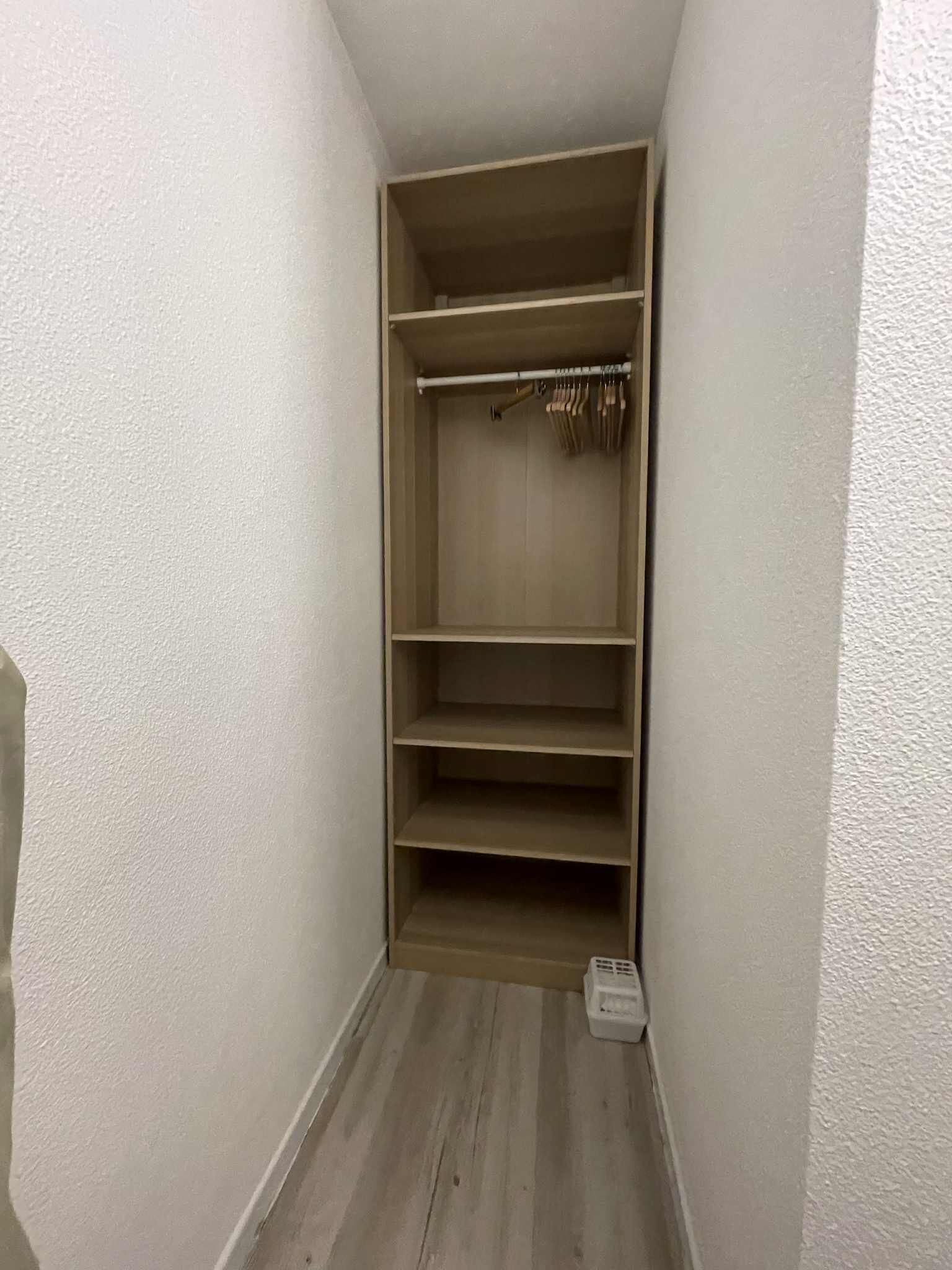 A narrow hallway with a wooden closet containing multiple shelves and hanging space.