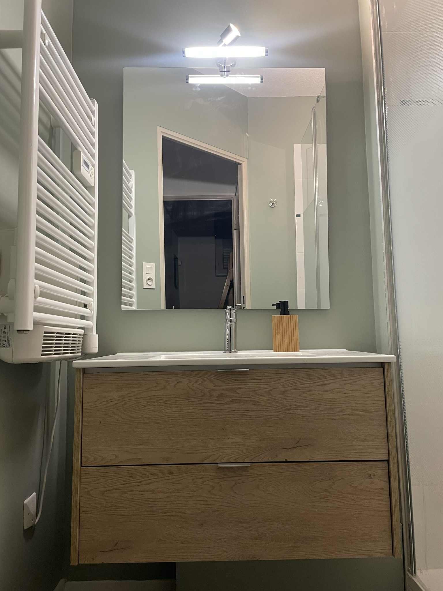 Un baño con tocador de madera, un espejo, un grifo y una lámpara en el techo.