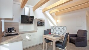 A modern kitchen with white cabinets, a built-in oven, and a microwave. There is a dining area with a table and two chairs. - Wohnung Bucki (Borkum)