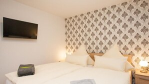 A neatly made bed with a patterned headboard, a flat-screen TV mounted on the wall, and a bedside table with a lamp. - Wohnung Bucki (Borkum)