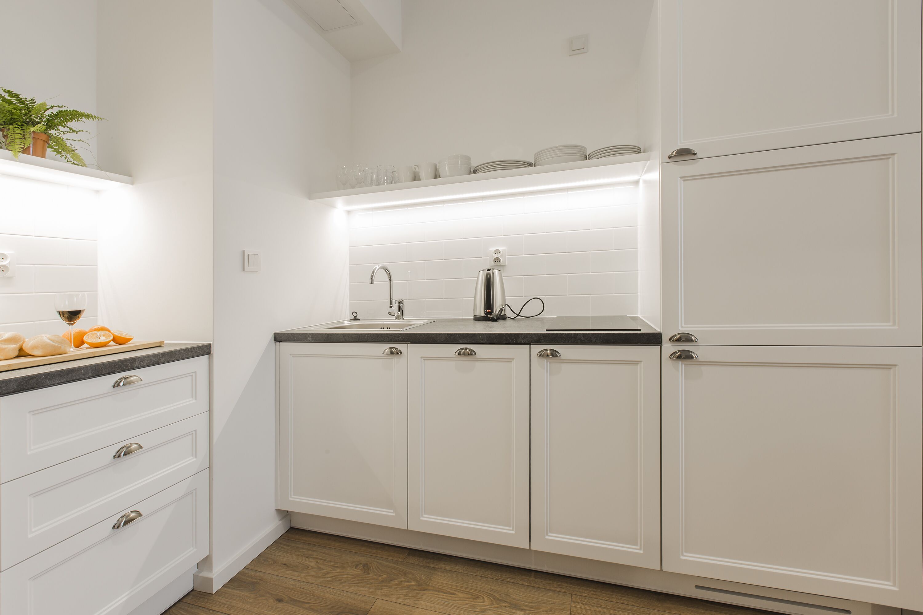 A kitchen with white cabinets, a countertop, and a sink. There are plates and glasses on the countertop.