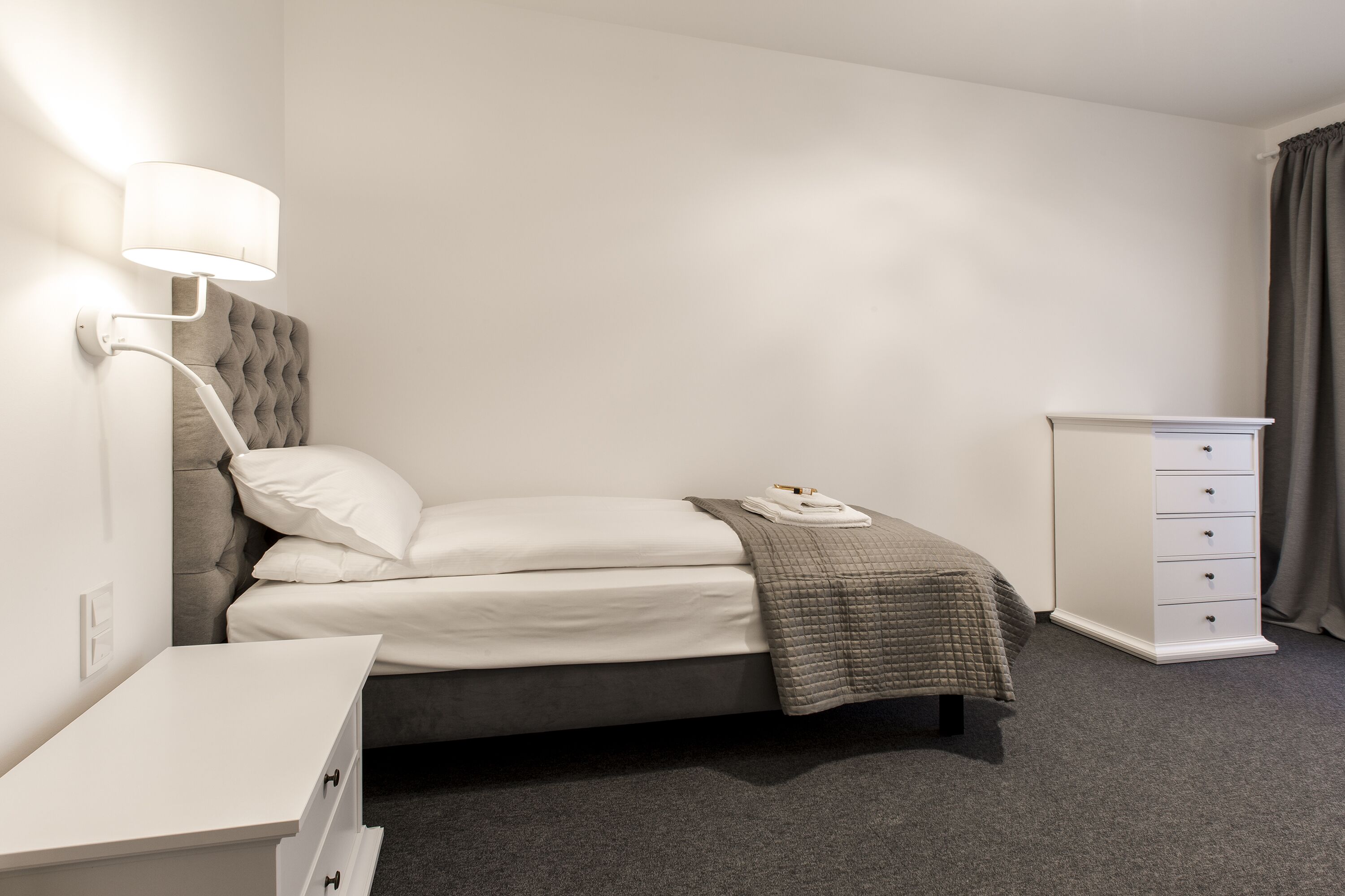 Un dormitorio ordenado con cama, mesita de noche, lámpara y cómoda.