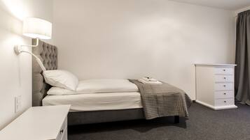 Un dormitorio ordenado con cama, mesita de noche, lámpara y cómoda.