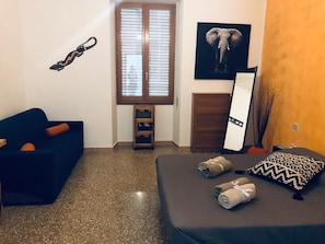 A room with a bed, a blue sofa, a wooden cabinet, a mirror, and a wall-mounted elephant picture. - Cimarosa Room (Cagliari)