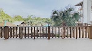 A fenced outdoor area with a pool, palm trees, and a building in the background. - Vitamin Sea - 3BR/3BA Redfish Village Condo - Sleeps 9 - Deeded Beach Access (Santa Rosa Beach)