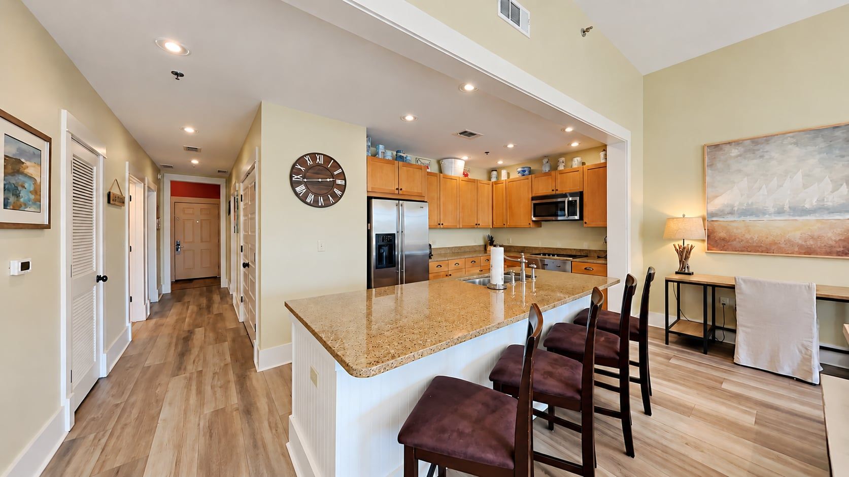 A modern kitchen with a central island, wooden cabinets, and a large clock on the wall.