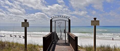 A wooden boardwalk leading to a beach with caution signs indicating a 15-foot drop.