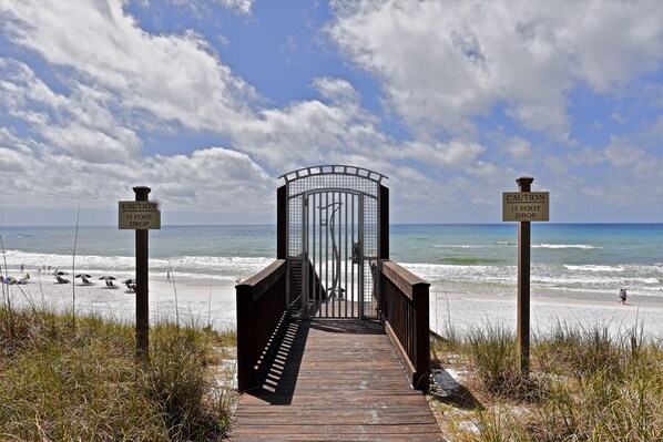 A wooden boardwalk leading to a beach with caution signs indicating a 15-foot drop.