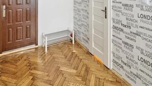 A room with a herringbone wooden floor, a wooden door, and a wall with repeated city names. - Dream Apartments Rzeszowska (Kraków)