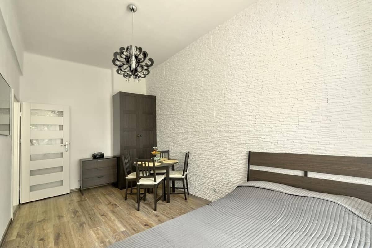 Um quarto com cama, guarda-roupa de madeira, mesa de jantar e cadeiras, e um candelabro.