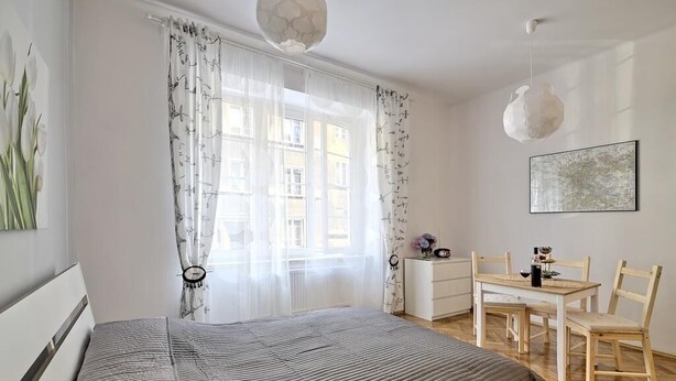 A bedroom with a bed, a bedside table, a chair, a table with chairs, and a window with curtains. - Dream Apartments Rzeszowska (Kraków)