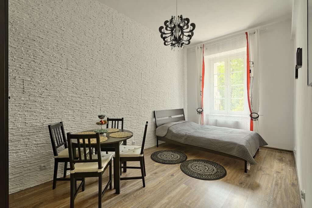 A room with a bed, a dining table with chairs, a chandelier, and a window with curtains.