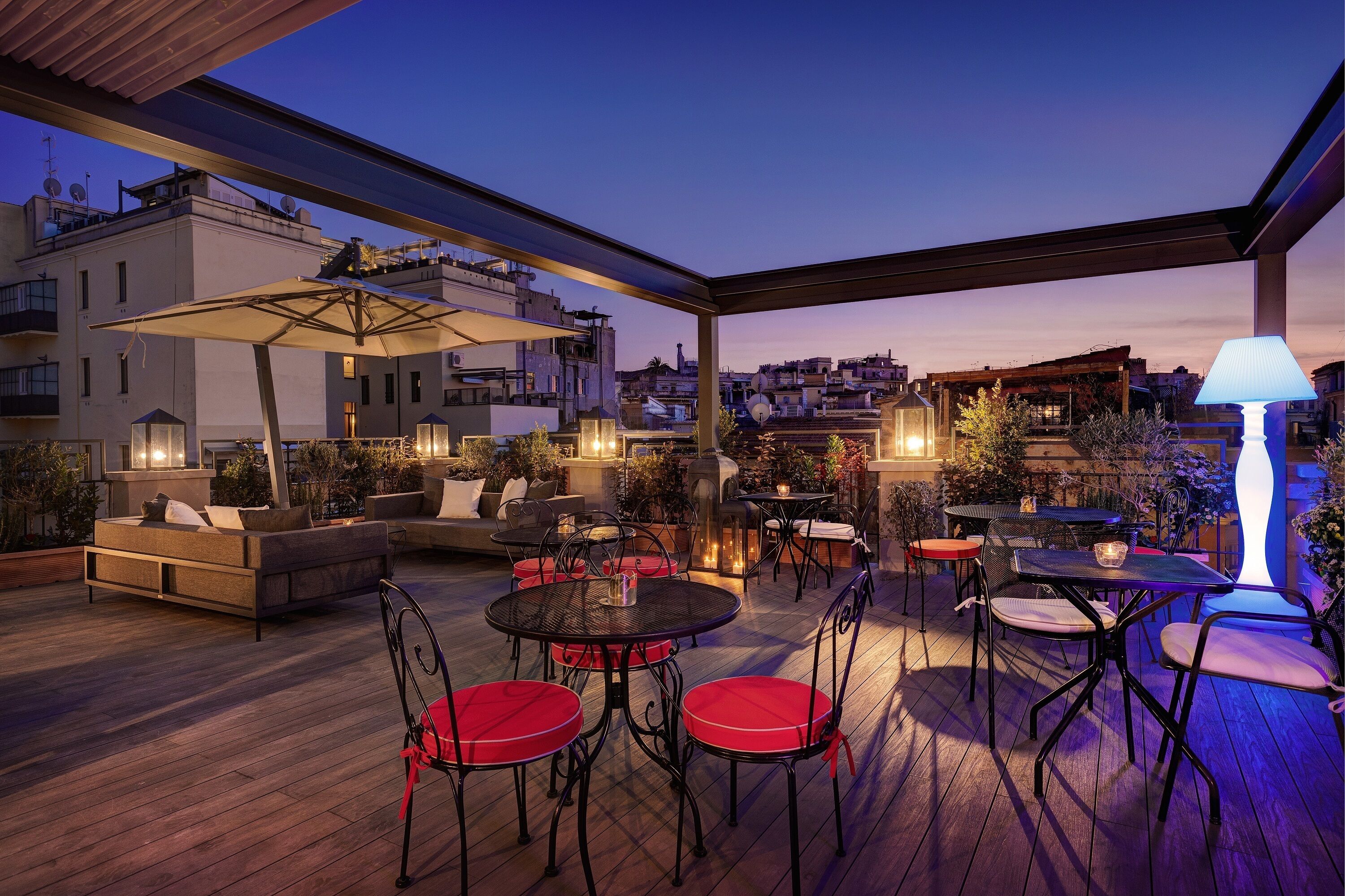 An outdoor patio with a wooden deck, red and black metal chairs, a round table, and a large umbrella.
