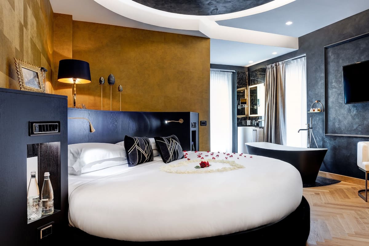 Una habitación de hotel moderna con una cama grande, una bañera negra y un televisor de pantalla plana en la pared.