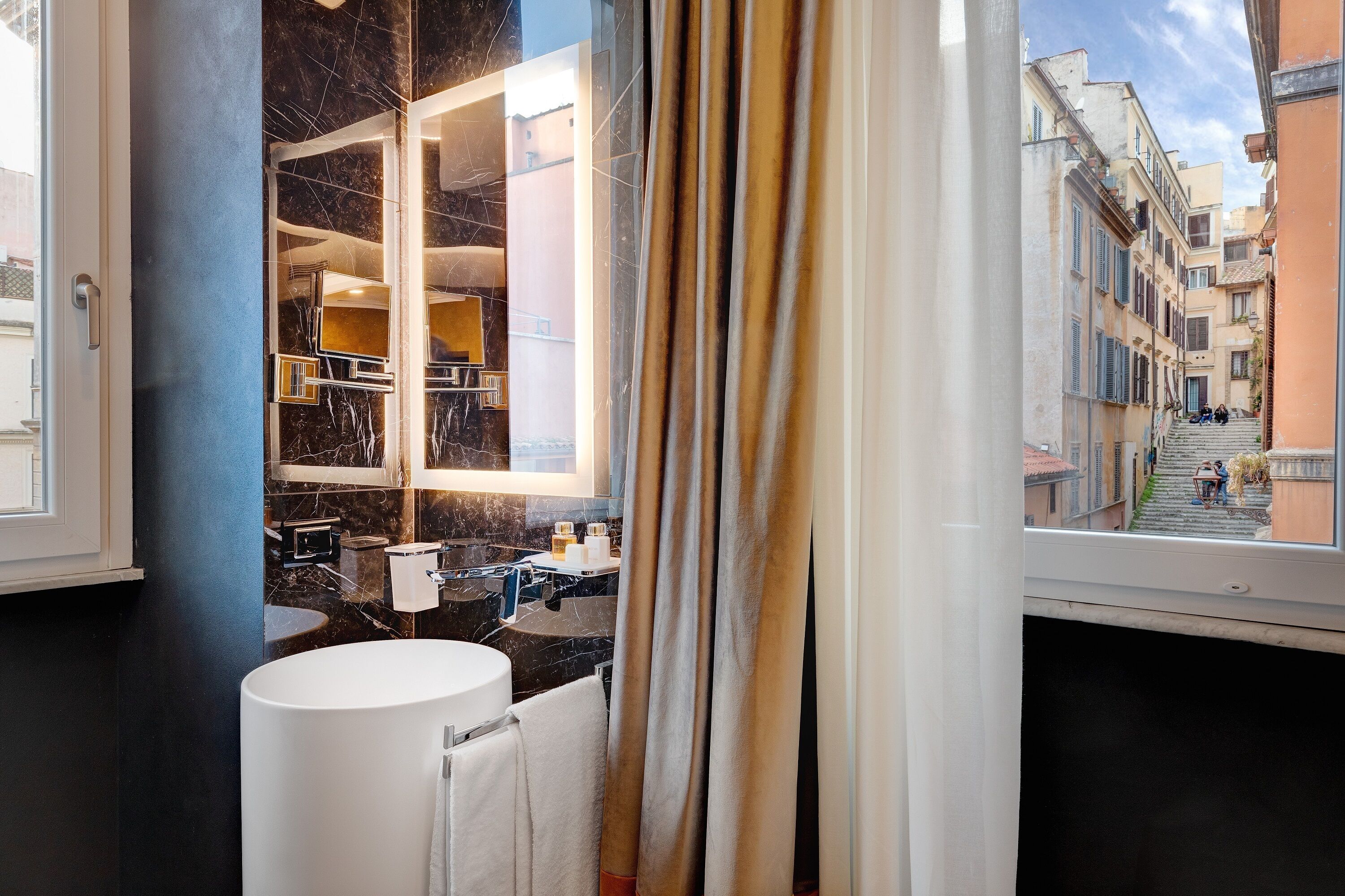 A modern bathroom with a large mirror, a round sink, and a view of a narrow street outside.