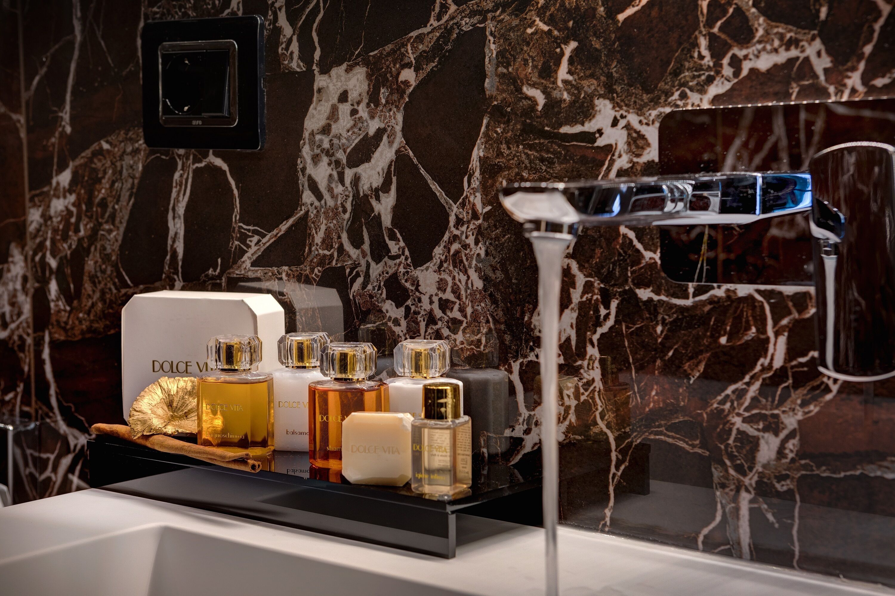 Une salle de bain avec un lavabo en marbre, un miroir et une collection de flacons de parfum Dolce Vita.
