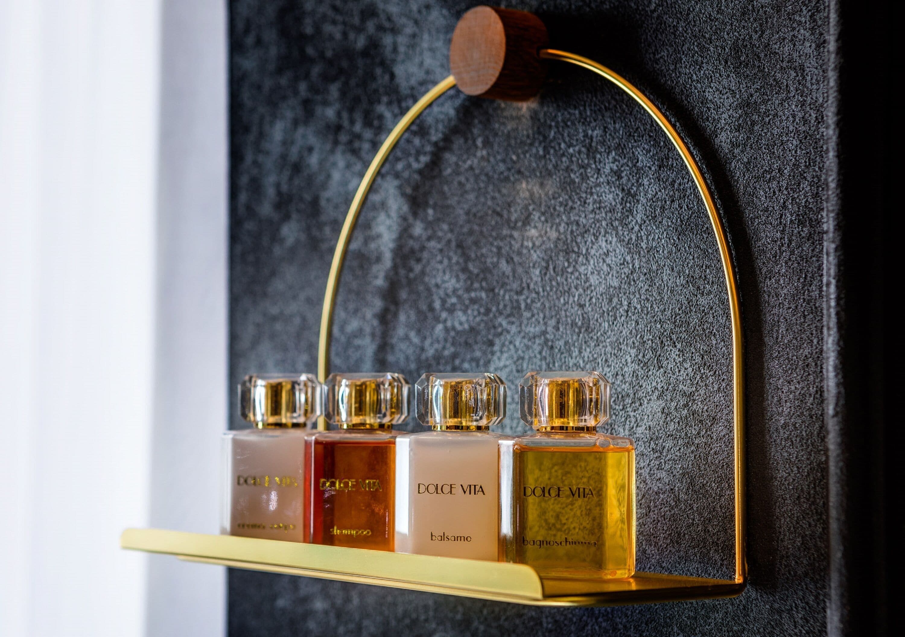 A display of Dolce Vita perfume bottles on a gold shelf against a dark textured wall.