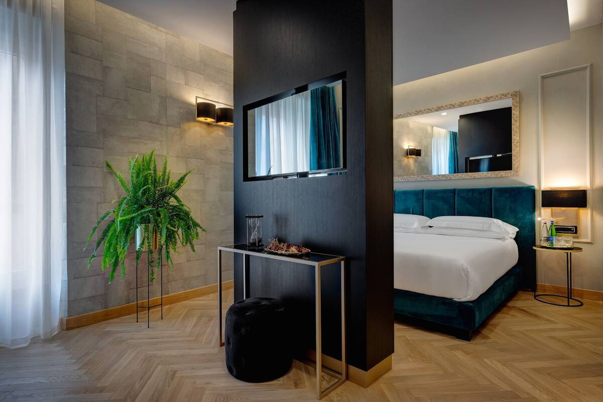 Habitación de hotel moderna con una cama grande, un espejo, una mesita con una planta y un televisor montado en la pared.