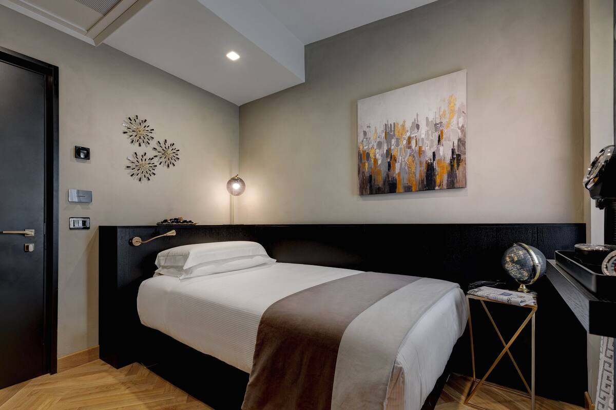 Habitación de hotel ordenada con cama, escritorio, un globo terráqueo y un cuadro en la pared.