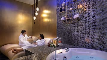 Un espace spa comprenant une grande baignoire, un coin salon avec une table et un mur décoratif orné de mosaïques.