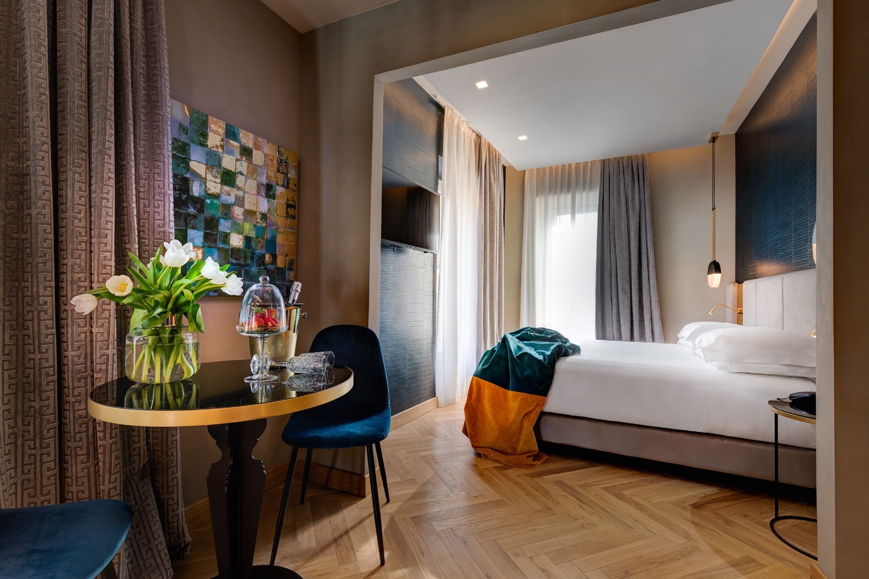 A hotel room with a bed, a table with a vase of flowers, a chair, and a wall with a checkered pattern.
