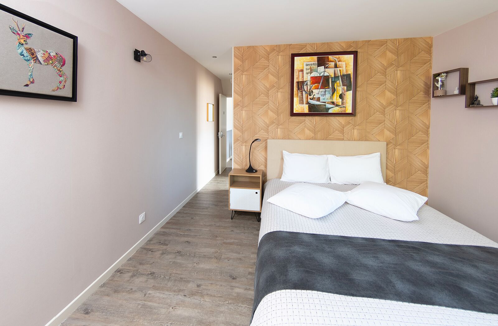 Moderni hotellihuone, jossa on suuri sänky, puinen pääty, yöpöytä ja seinälle kiinnitetty taideteos.