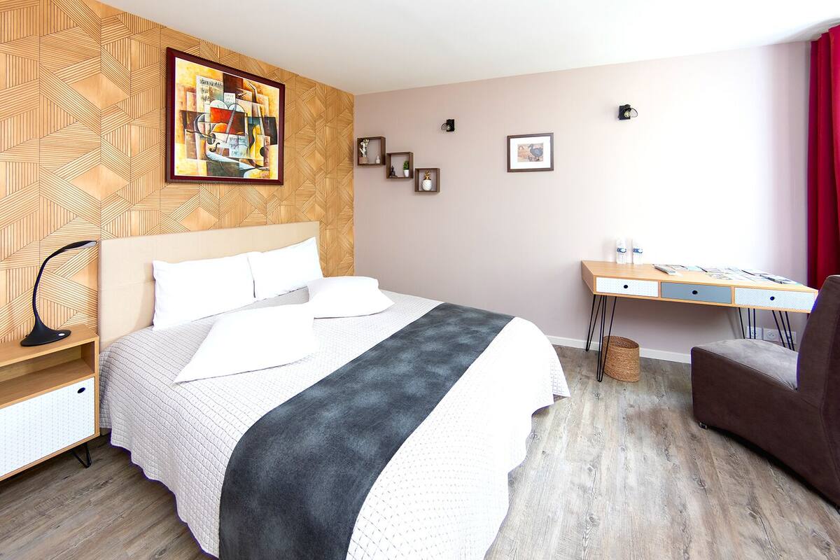 A neatly arranged bedroom with a bed, bedside table, desk, and chair.