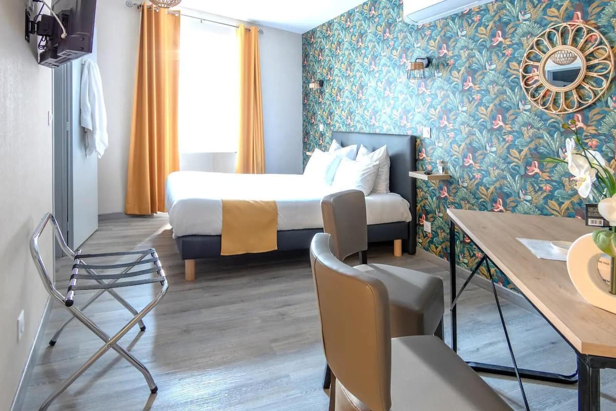 A hotel room with a bed, a desk, a chair, a TV, and a shower area.