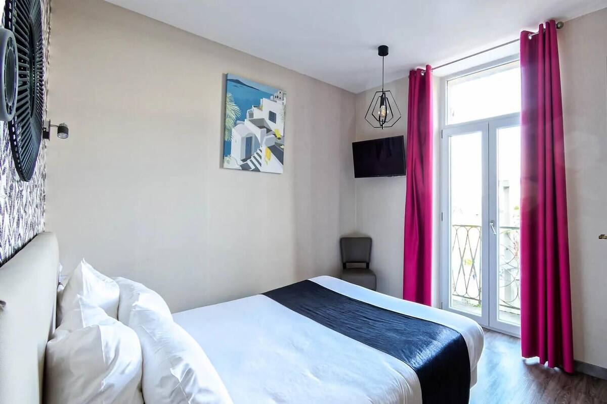 A bedroom with a bed, a painting, a TV, and a balcony with curtains.