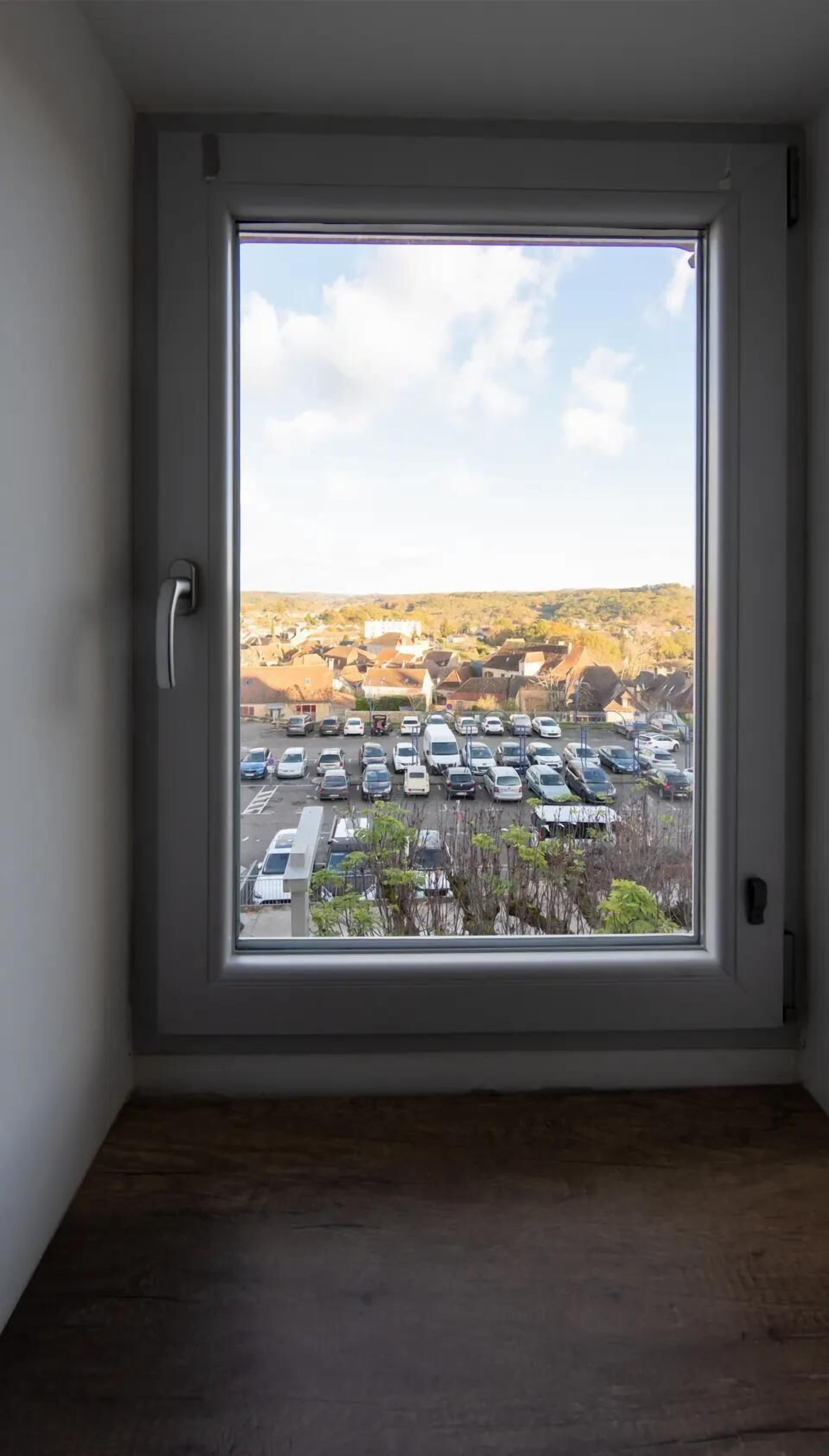 Ein Zimmer mit großem Fenster und Blick auf einen Parkplatz sowie Gebäude.