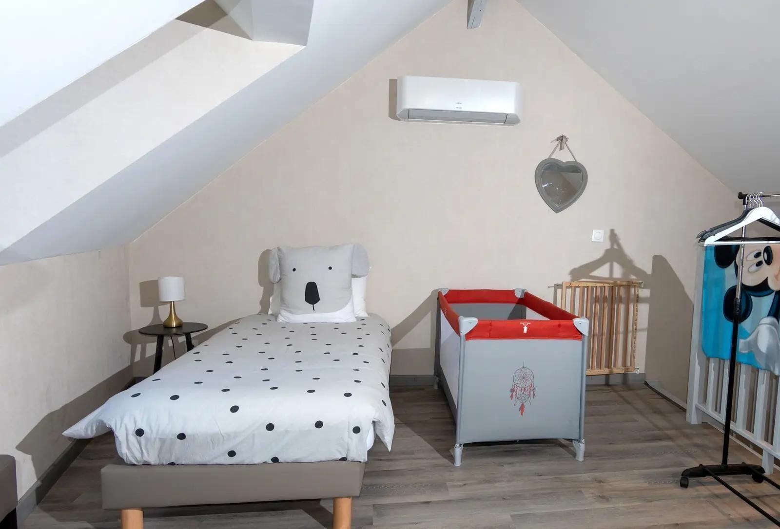 A bedroom with a bed, a crib, a hanging heart-shaped decoration, and a wall-mounted air conditioner.