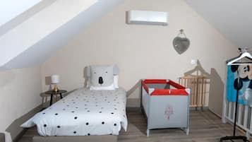 A bedroom with a bed, a crib, a hanging heart-shaped decoration, and a wall-mounted air conditioner.