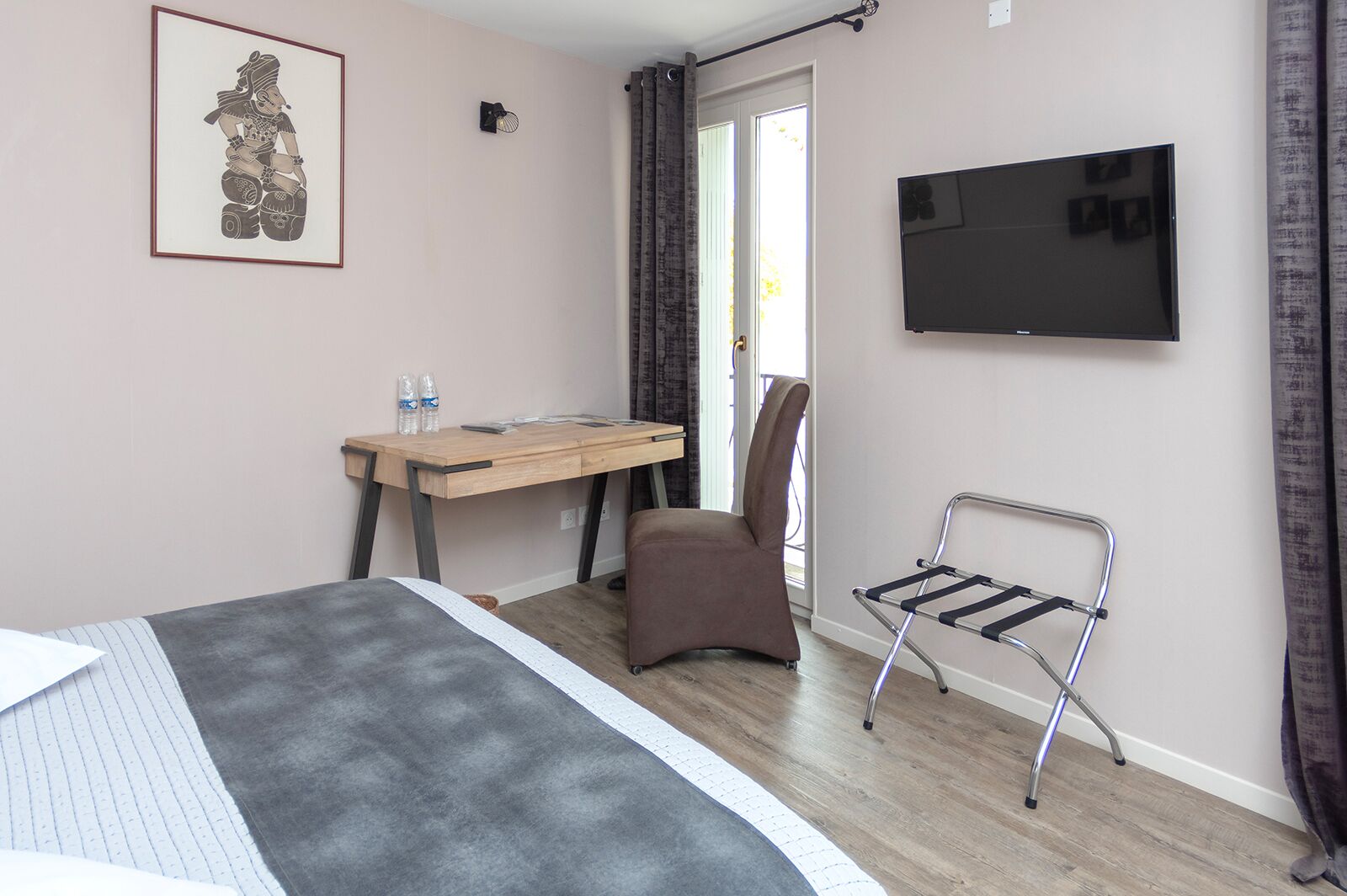 Quarto de hotel com cama, escrivaninha, cadeira, televisão e janela com cortinas.