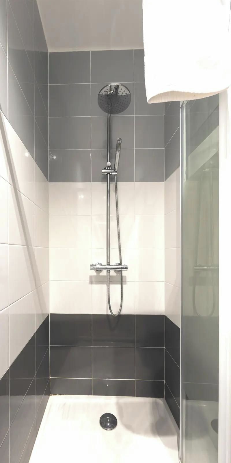 Een moderne douchecel met glazen wanden, een handdouche en een bedieningspaneel aan de muur.